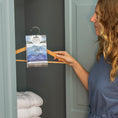 Load image into Gallery viewer, A woman hangs a Fresh Scents Adventure Mountain - Sachet 3pk on a wooden hanger in a light blue cabinet, bringing long-lasting freshness to the space with neatly folded white towels.
