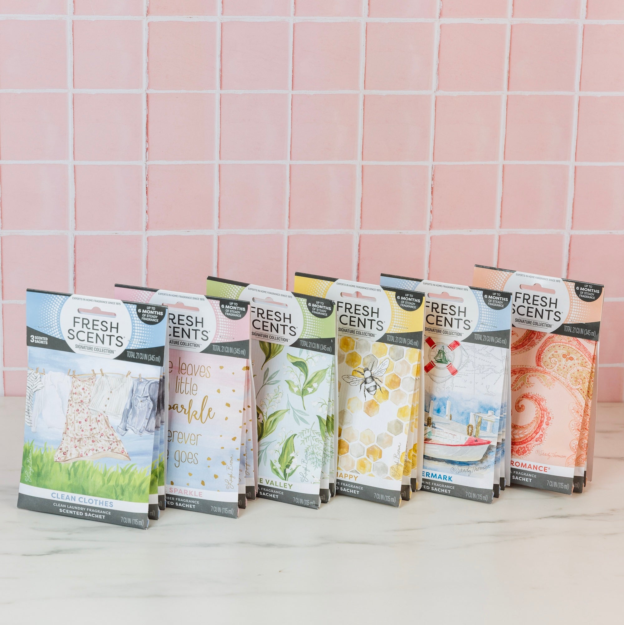 Six Bestsellers Bundle scented sachets by Fast Bundle are displayed in colorful packaging on a white surface with a pink tiled wall behind. This charming set features assorted air freshener scents and unique designs.