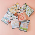 Load image into Gallery viewer, Six Bestsellers Bundle scented sachets by Fast Bundle in colorful packs are displayed on a light pink surface. Scents featured include Watermark, Clean Clothes, Summer Romance, Little Sparkle, and two additional fragrances.
