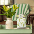 Load image into Gallery viewer, A ceramic vase with white lilies and a Fresh Scents Lily of the Valley - Sachet 3pk rests on a mint-green tray. In the background, a green and white striped blanket is draped over a brown couch.
