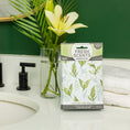 Load image into Gallery viewer, A box of Fresh Scents Lily of the Valley - Sachet 3pk, a flameless air freshener with long-lasting fragrance, sits on a bathroom counter beside yellow lilies, a black faucet, a sink, and folded white towels against a green wall.
