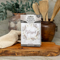 Load image into Gallery viewer, A box labeled Fresh Scents Blessed Wreath 3pk sits on a wooden board, offering flameless fragrance, with a tan towel, wooden utensils in a ceramic pot, and green foliage in the background on a kitchen counter.
