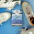 Load image into Gallery viewer, A blue Fresh Scents Adventure Mountain Sachet 3pk lies on a blue surface, surrounded by three pairs of white and beige sneakers, providing long-lasting freshness.
