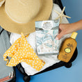 Load image into Gallery viewer, An open suitcase with a straw hat, yellow floral swimsuit, starfish, Sun Bum sunscreen, and Fresh Scents Painted Palm - Sachet 3pk for a flameless fragrance. A hand places the long-lasting air freshener sachets inside.
