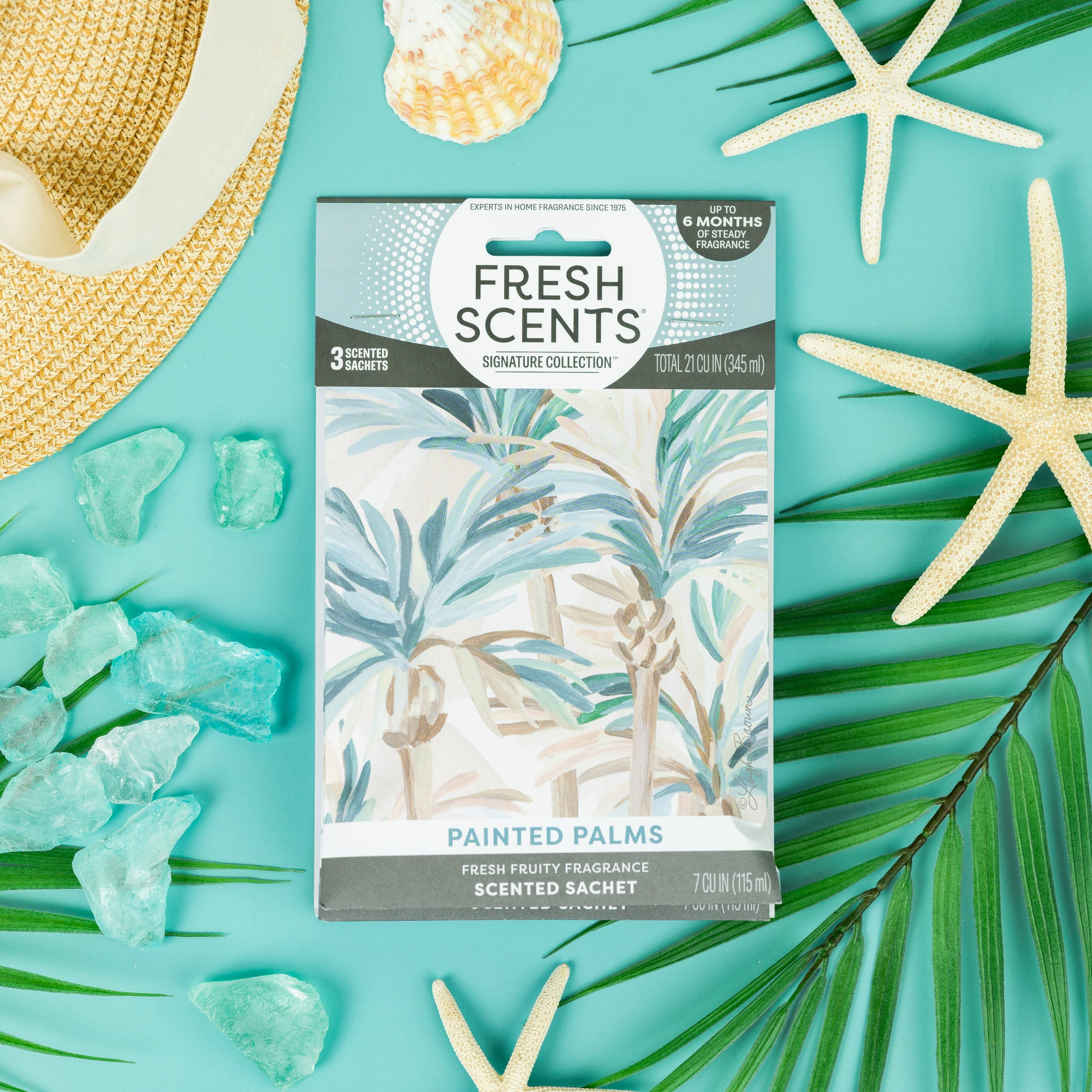 The Fresh Scents Painted Palm - Sachet 3pk features a palm design and offers flameless fragrance, shown on a turquoise background with sea stars, palm leaves, sea glass, and a straw hat for a tropical vibe.