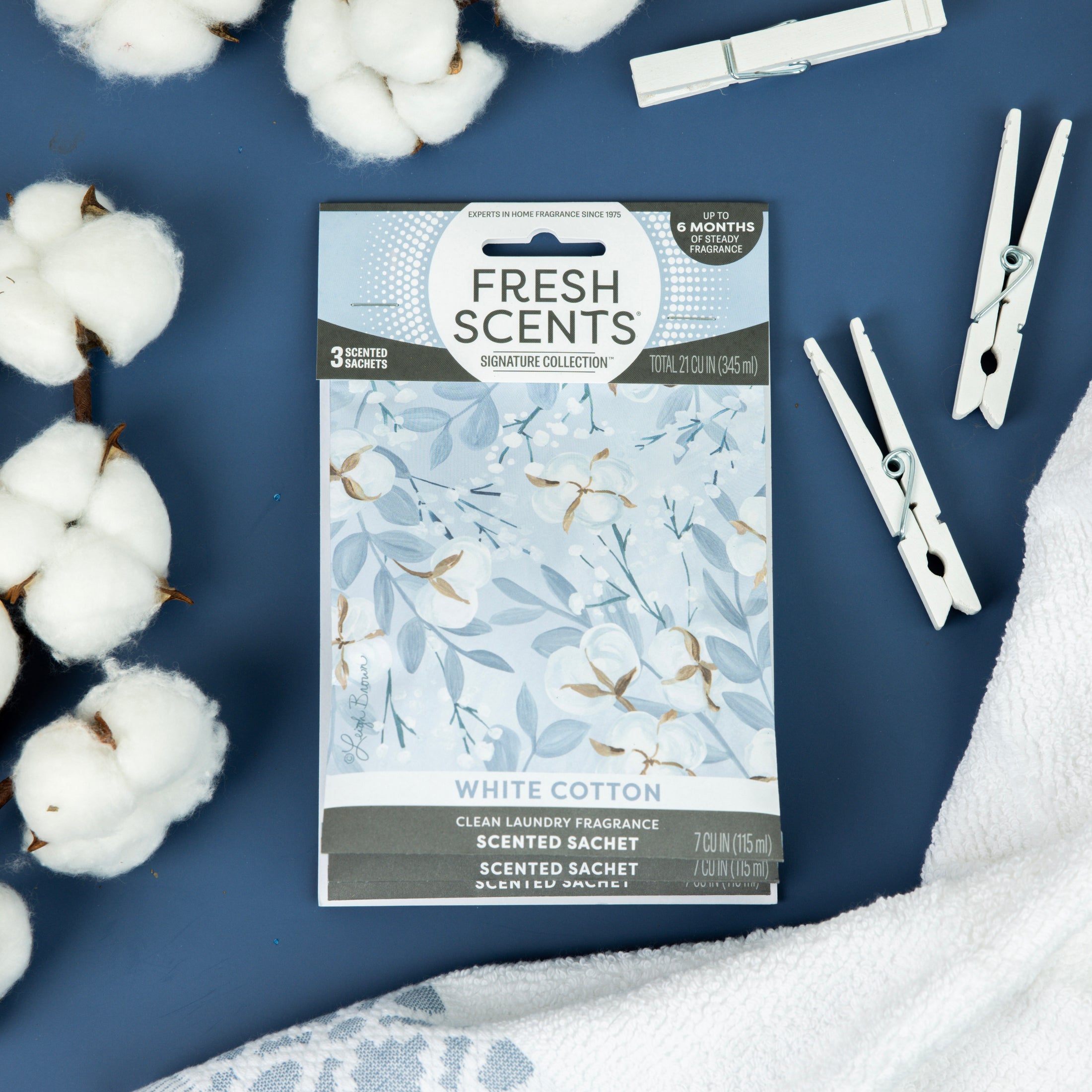 A Fresh Scents White Cotton - Sachet 3pk is displayed on a blue surface with cotton stems, a towel, and clothespins, capturing the fresh laundry vibe of this long-lasting flameless air freshener.