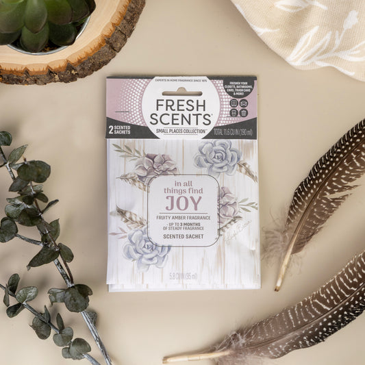 The Fresh Scents In All Things - Sachet 2pk features a floral design and uplifting quote, displayed with feathers, eucalyptus, a wooden coaster, and patterned cloth—ideal for adding fragrance to small spaces.