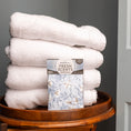 Load image into Gallery viewer, A stack of four white towels sits on a wooden tray. In front is Fresh Scents White Cotton - Sachet 3pk, a flameless air freshener with a floral design featuring white flowers and green leaves for long-lasting fragrance.
