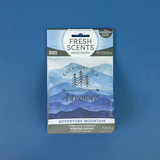 A Fresh Scents Adventure Mountain - Sachet 3pk, featuring blue mountain artwork and the phrase "Everyday is a new adventure," rests on a blue surface, emphasizing long-lasting freshness.