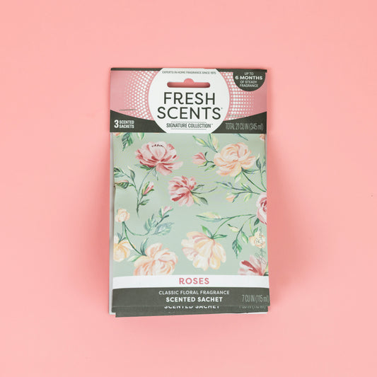 A Fresh Scents Roses - Sachet 3pk lies on a pink background. The floral box features pastel roses and green leaves, promising long-lasting fragrance. Each package includes three flameless scented sachets.
