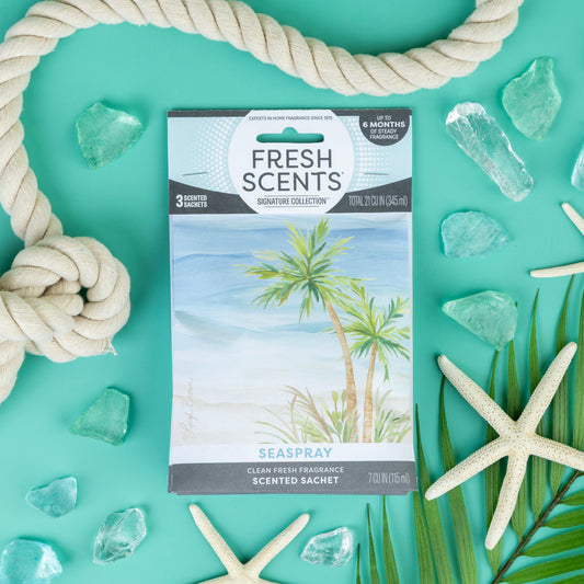 A Fresh Scents Seaspray - Sachet 3pk rests on turquoise with rope, glass, leaves, and starfish accents. Enjoy this flameless fragrance, packaged with palm trees by the ocean for a refreshing scent experience.