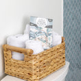 Load image into Gallery viewer, A woven basket with rolled white towels and Fresh Scents Painted Palm - Sachet 3pk sits on a white surface before blue patterned tiles, adding a flameless fragrance to the space.
