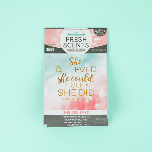 The Fresh Scents She Believed - Sachet 3pk features pink and white scented sachets with a fruity floral fragrance, accented by gold text: "She believed she could so she did." Perfect for long-lasting, flameless air freshening.