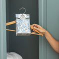 Load image into Gallery viewer, A hand places a Fresh Scents White Cotton - Sachet 3pk into a blue closet. Folded white towels sit on a lower shelf, enhancing the clean atmosphere with this flameless air freshener.
