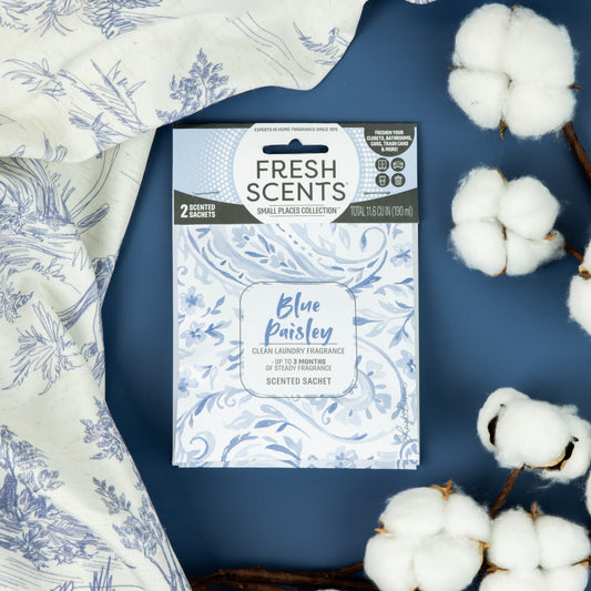 A Fresh Scents Paisley - Sachet 2pk rests on a blue surface with white cotton branches and patterned fabric, all in a blue and white floral design—a perfect air freshener for small spaces.