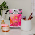 Load image into Gallery viewer, A pink and white Hello Gorgeous - Sachet 3pk by Fresh Scents sits on a bathroom counter, providing long-lasting fragrance beside a makeup brush cup, glass dropper bottle, and a cream jar with a pink applicator.
