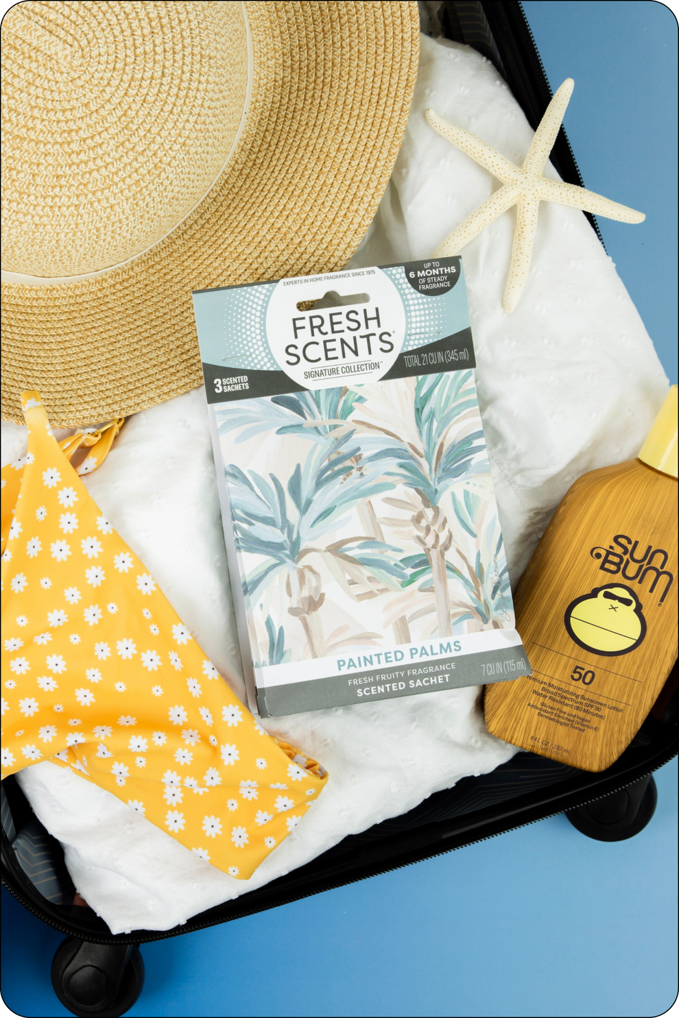 A suitcase packed with a straw hat, a box of Fresh Scents sachets, a starfish, yellow floral swimwear, and a bottle of Sun Bum SPF 50 sunscreen on a blue background.